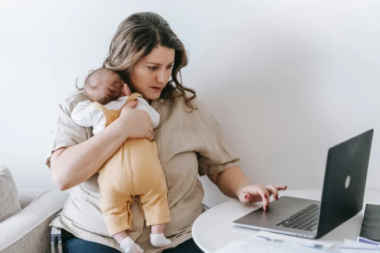 Femme débordée en télétravail avec son bébé dans les bras et devant son ordinateur, et qui voudrait trouver des solutions pour retrouver un meilleur équilibre vie privée, vie professionnelle.
