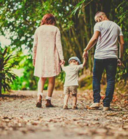 Jeunes parents qui tiennent par la main leur enfant qui apprend à marcher et qui se sont fait accompagner par la sophrologie, près de Rouen, pour aborder, dans leur vie d'adulte, leur nouvelle parentalité plus sereinement.