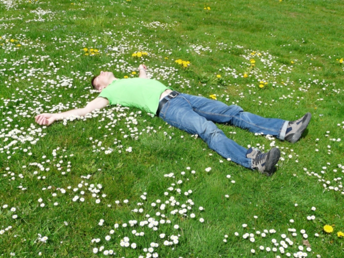 Un homme allongé dans l'herbe qui prend le temps de vivre et de profiter de l'instant présent, après avoir fait un suivi en sophrologie près de Rouen et compris que mieux valait prendre plusieurs pauses plutôt que de courir toute la journée.